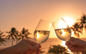Two wine glasses at sunset on the beach with palm trees in the background