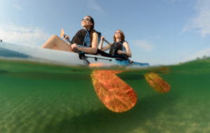 Two women in life jackets and blue kayak in the ocean
