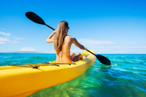 Girl with long hair paddling in a yellow kayak in the ocean