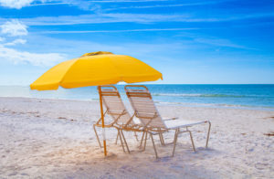 Two beach chairs under a large yellow umbrella in the white sand on siesta key beach