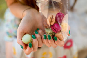 Girl with green nails holding a bag of colorful macarons