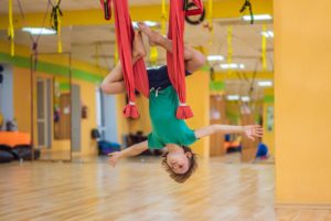 Young kid hanging on red aerial silks