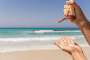 Male hands with sunscreen on beach background.