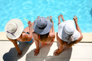 three women wearing hats sitting by a pool