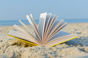 An open book laying on a sandy beach.