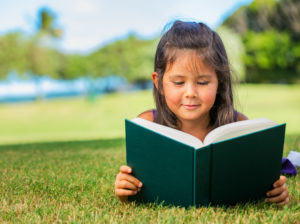 Cute Little Girl Reading Outside on Grass