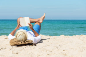 A handsome man relaxing on a book reading on the beach.