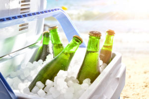 Bottles of beer chilled on ice in a camping fridge on a beach on a hot day with sunshine.