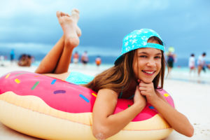 Young girl with a blue hat longing on a pink doughnut pool float on the sandy beach