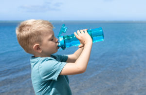 Child drinking water from bottle at the beach.