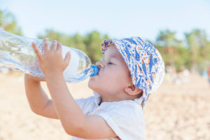 Little boy drinking from a large water bottle at the beach