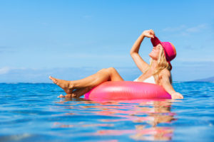 Beautiful girl floating on a pink raft in tropical ocean