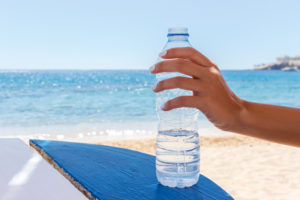 female hands holding a water bottle on the beach.