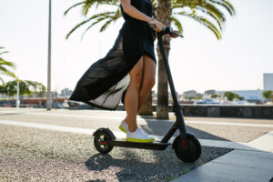 Young beautiful woman in a black dress riding an electric scooter to work, female legs on electric scooter, electric transport, ecology, ecological transport, sunset, electric skateboard, 4k - Imagen
