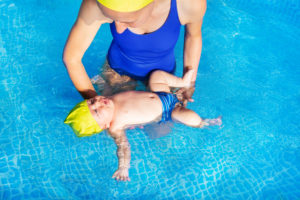 Baby learning to float on his back in the pool during a swim lesson.