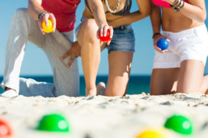 Group of young people playing boule on beach in sand outdoors in summer