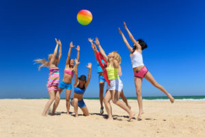 Group of young joyful girls playing volleyball on the beach