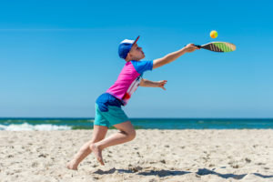 Young boy playing tennis on beach. Summer sport concept