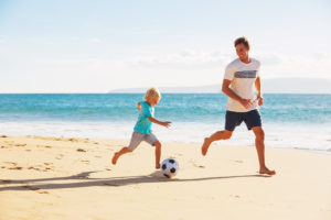 Happy Father and Son Having Fun Playing Soccer on the Beach