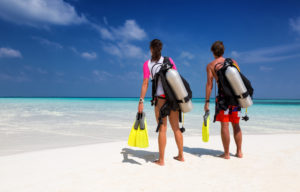 Young couple in scuba diving gear on a tropical beach