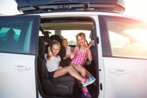 Group of three cute adorable little happy caucasian children enjoy having fun sit in minivan going to sea beach road trip on hot summer day. Kids in swimsuit in car with side open door against sun