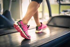 Fitness girl running on treadmill. Woman with muscular legs in gym