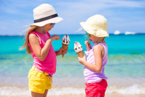 Happy little girls eating ice-cream over summer beach background. People, children, friends and friendship concept