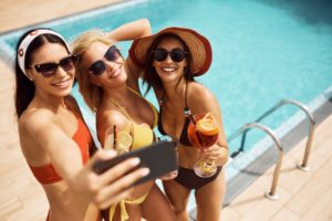 Happy female friends having fun while taking selfie on cocktail party at swimming pool. Copy space.