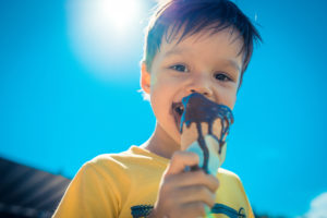 3 year old asian caucasian boy enjoying a melting chocolate ice-cream on a sweltering hot summer day. Clear blue summer sky in background
