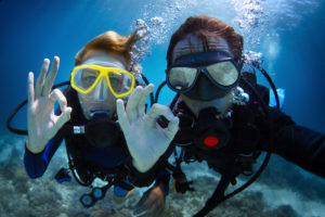 Underwater shoot of a young couple diving with scuba in a tropical sea and showing ok signal