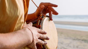 Man playing on a drum with his hands on the sandy beach, close up. Hands tapping a small drum outdoor