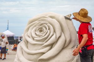 SARASOTA, FLORIDA, USA - NOV. 12, 2021: An artist with a trowel smooths part of a floral sculpture in progress Siesta Key Crystal Classic, an international sand sculpting festival on Siesta Key Beach.