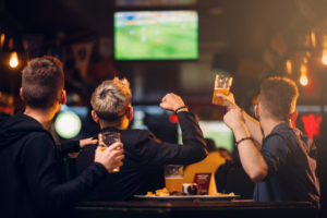 Three,Men,Watches,Football,On,Tv,In,A,Sport,Bar