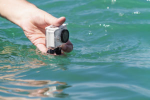 A man is taking photo and video above the water on action camera in underwater case. Closeup, selective focus